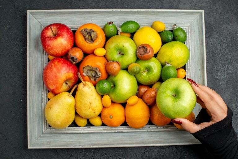 Above view of hand taking one of apples from collection of fresh fruits in picture frame on dark background